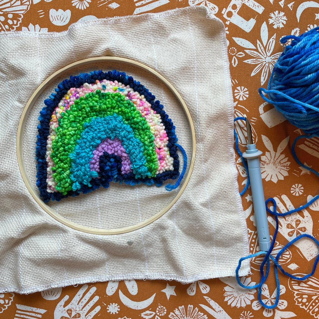 punch needle rainbow in progress on canvas with blue punch needle